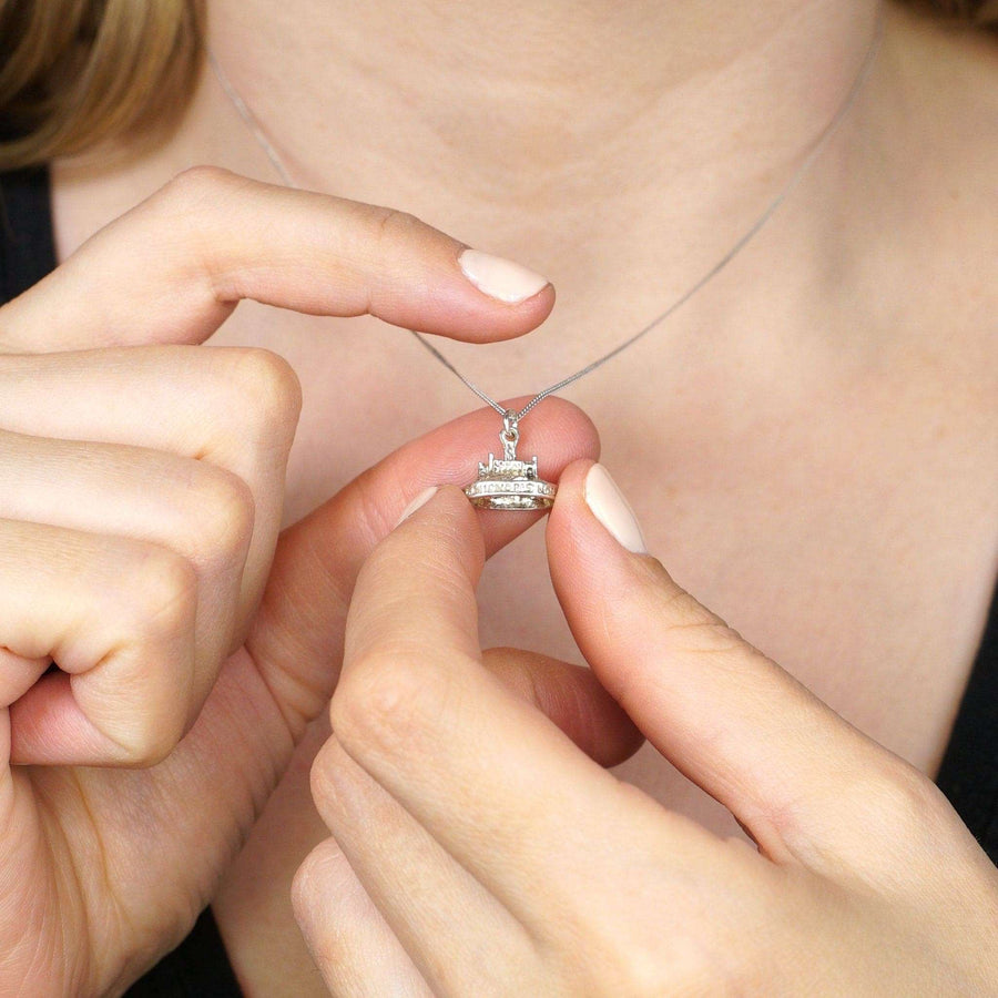 Close-up of a person holding a vintage silver Saint Michael's Mount charm pendant on a delicate necklace.