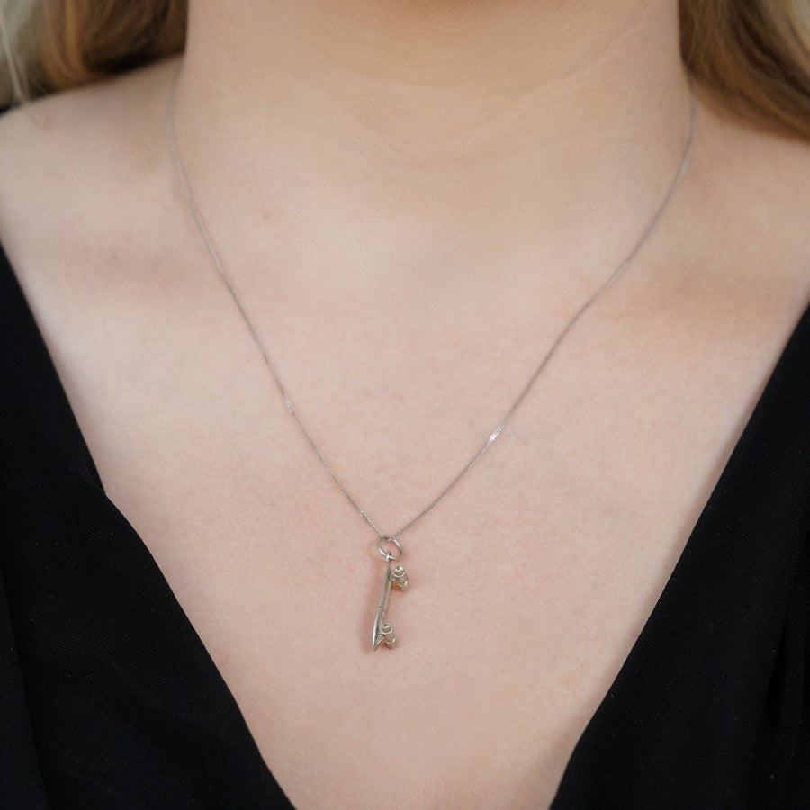 Close-up of a vintage silver skateboard pendant charm necklace worn on a stylish black top.