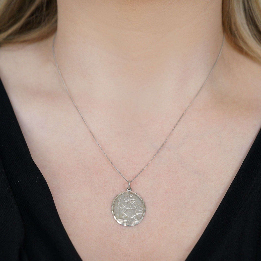 Vintage silver St Christopher pendant on a delicate chain, worn by a person, symbolizing protection for travelers.