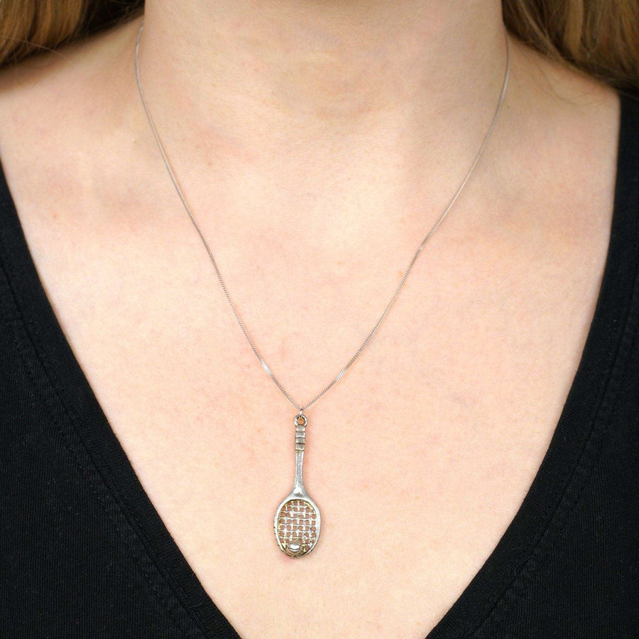 Vintage silver tennis racket and ball pendant worn on a woman's neck, perfect for tennis lovers.