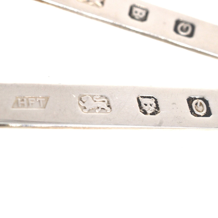 Close-up of vintage sterling silver shirt collar stiffeners showing hallmark stamps and intricate details.